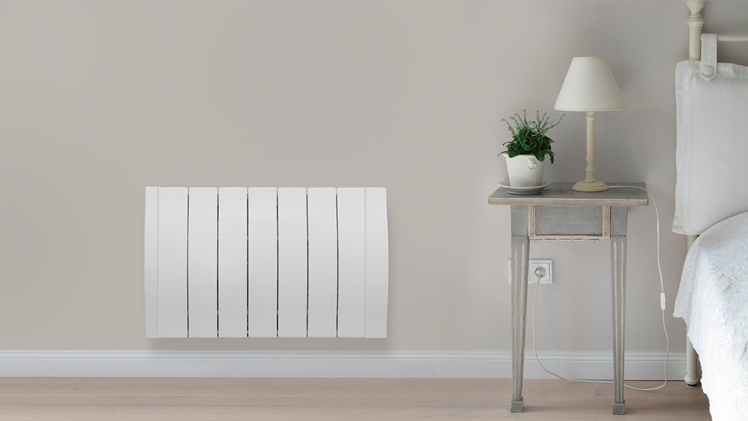 mejores-radiadores-electricos Uno de los radiadores eléctricos de color blanco en el dormitorio al lado de la mesita de noche