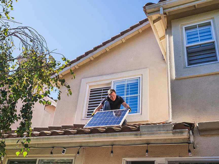 placas-solares-vivienda Hombre colocando una placa solar sobre el tejado de una vivienda unifamiliar