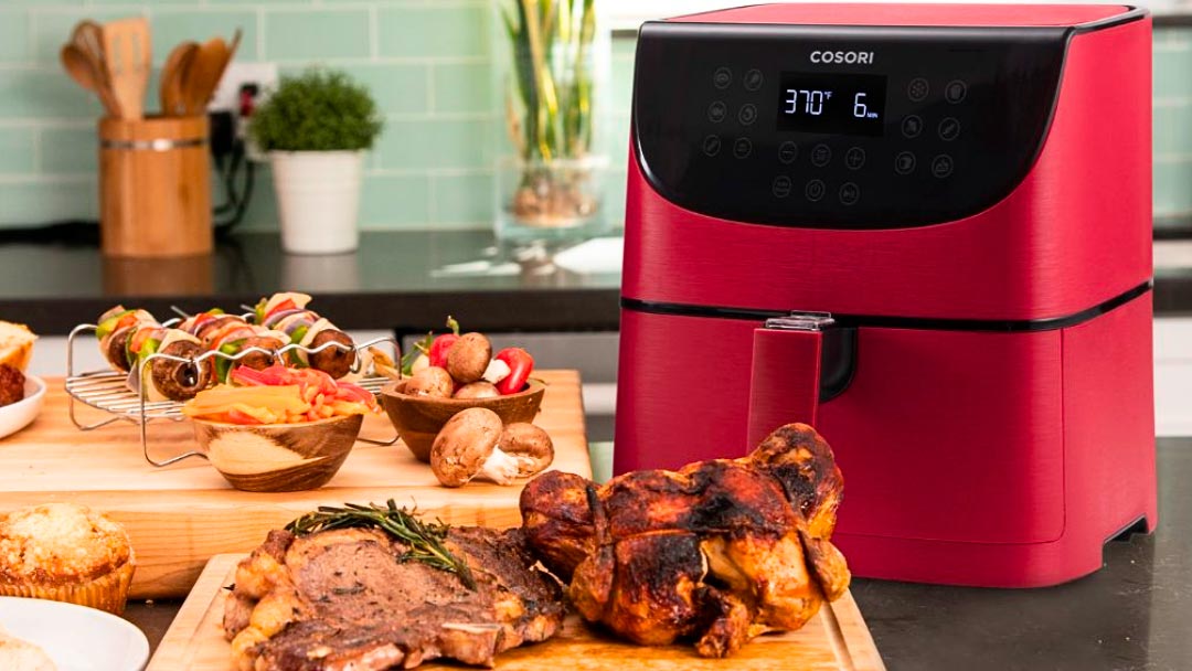 freidoras-sin-aceite-cosori una de las freidoras sin aceite Cosori de color rojo rodeada de alimentos en la cocina