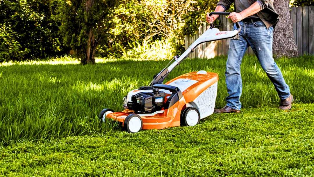 mejores-cortacesped-gasolina hombre manejando una de las cortacésped gasolina de color naranja en el jardín